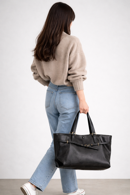 Person holding a black leather handbag against a plain background