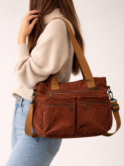 Brown handbag with a strap over shoulder worn by a person in a white sweater and blue jeans.