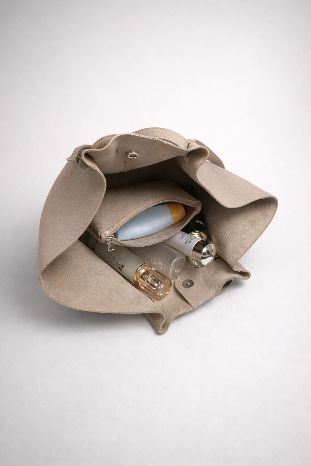 Beige leather bag with a mirror and other items on a white background