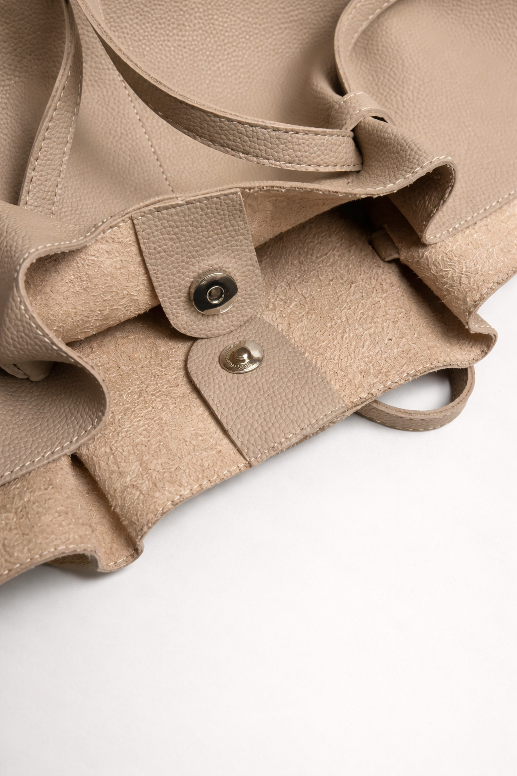 Close-up of a beige leather bag with buttons on a white background