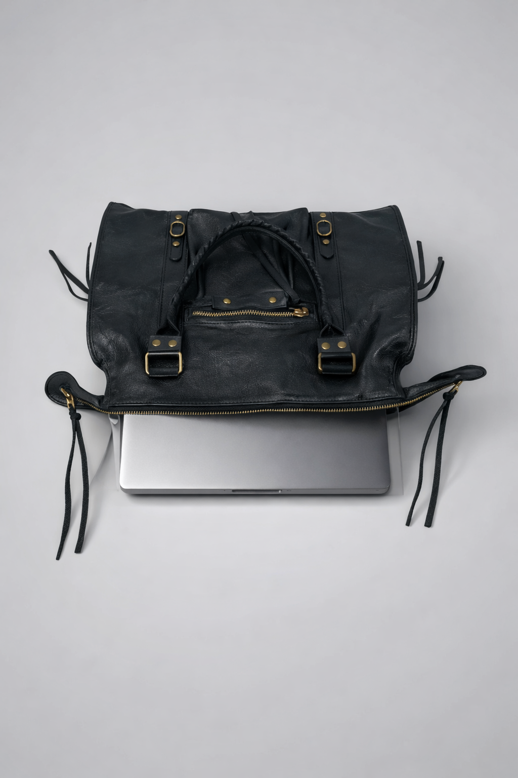 Black leather bag with gold buckles holding a laptop on a light gray background
