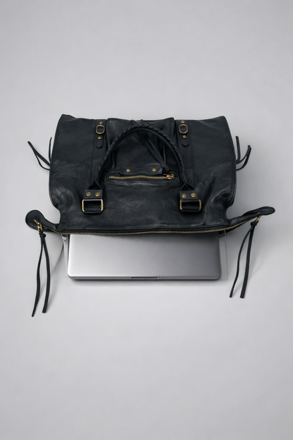 Black leather bag with gold buckles holding a laptop on a light gray background