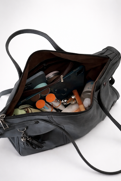 Black handbag with its interior open, showing various items on a white background