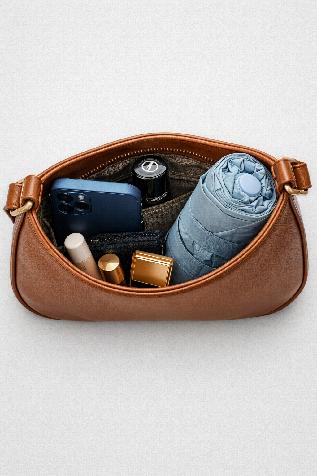 Brown leather bag with items including a phone, bottle, and umbrella on a white background
