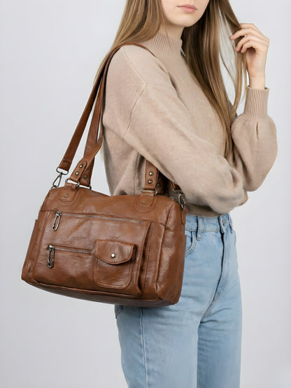 Woman holding a brown leather handbag against a plain background